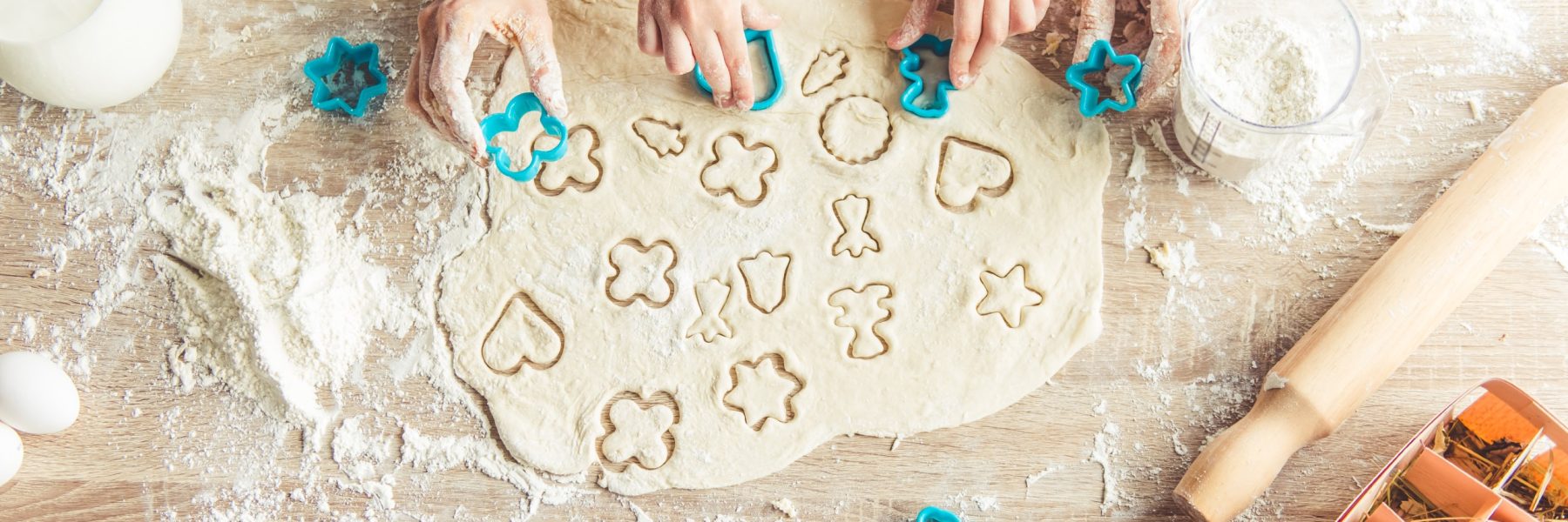 Top view of little girl and her mother preparing cookies using cookie cutters, cropped